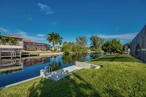 A tranquil outdoor pool area with a clear blue sky, a well-maintained lawn, and a modern building in the background.