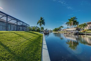 Un canal con un muelle para barcos, una zona verde y palmeras.
