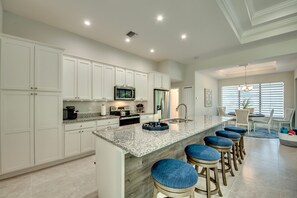 Una cocina moderna con gabinetes blancos, encimeras de granito y una isla central con taburetes de bar.