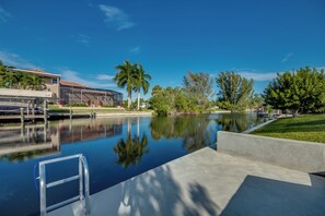 A swimming pool with a ladder, surrounded by palm trees and a building with a red roof.