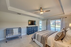 A bedroom with a large bed, a crib, a dresser, a ceiling fan, and a TV on the wall.