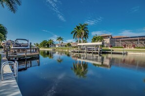 A calm water body with a dock and a boat, surrounded by palm trees and a building with a tiled roof.