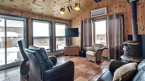 A cozy room with a fireplace, leather seating, a flat-screen TV, and large windows.