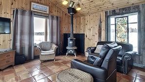 A cozy living room with wooden walls, a fireplace, leather sofas, and a television.