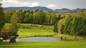 A golf course with a pond, trees, and mountains in the background.