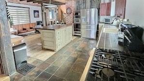A kitchen with a central island, stainless steel appliances, and a tiled floor.