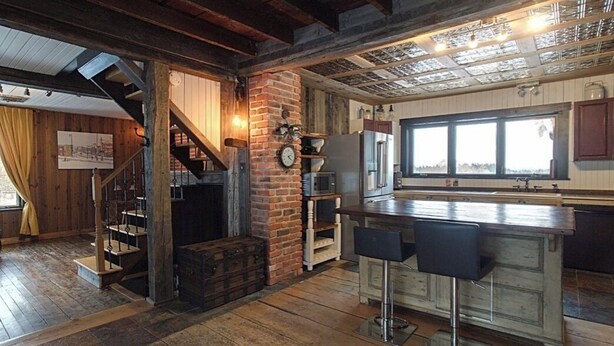 A rustic kitchen with a wooden staircase, a brick wall, and a large window.
