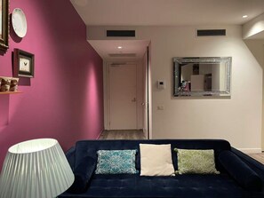A room with a dark blue sofa, a white lamp, and a mirror on the wall.