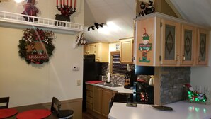 A kitchen with wooden cabinets, a black refrigerator, and a dining area with a red table and chairs. - Year Round Access in town Bungalow, Hot Tub, Fire Pit and Extra Parking      (Maggie Valley)