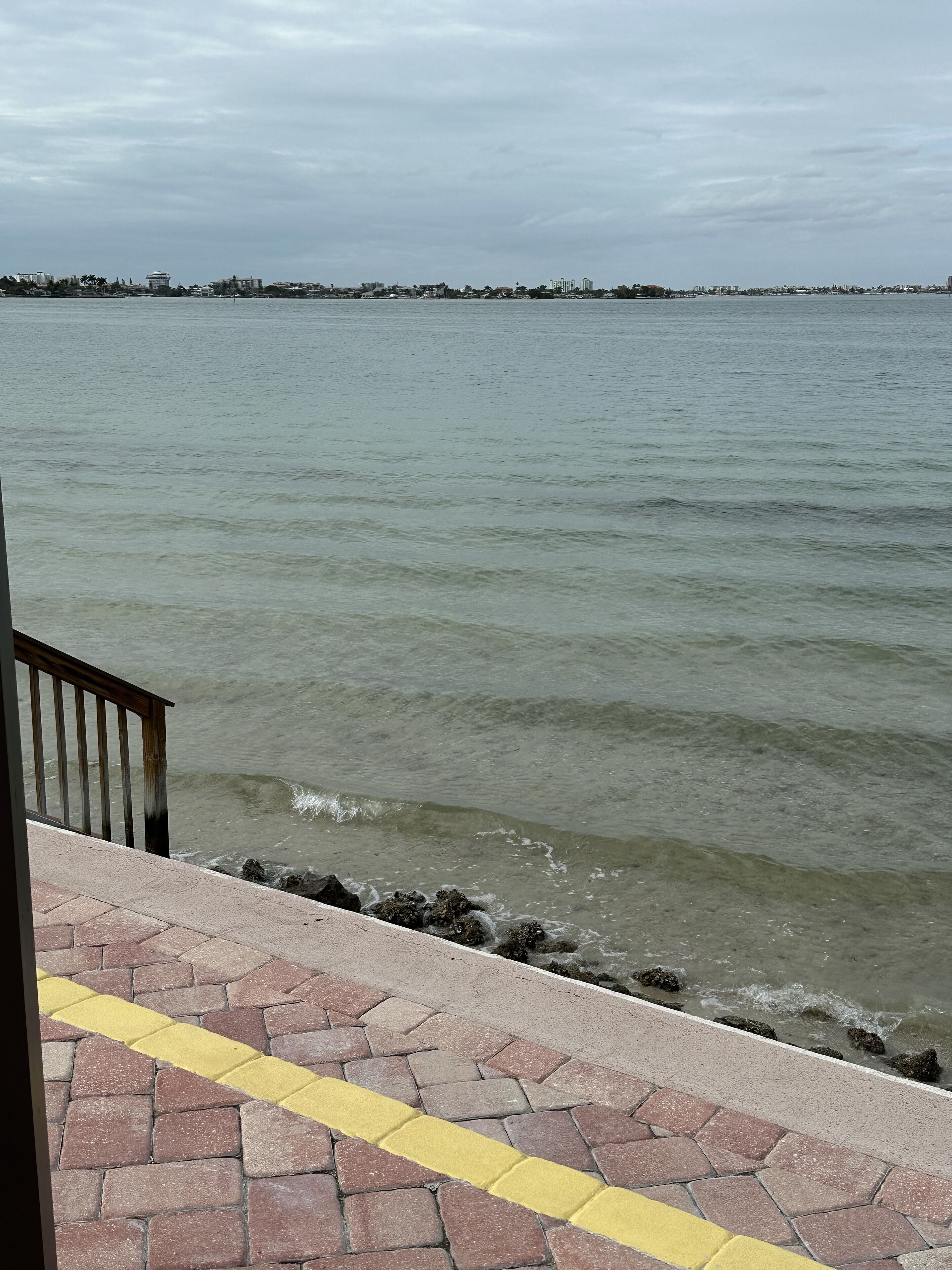 A waterfront view with a paved walkway and a railing.