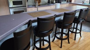 A kitchen with a central island, four bar stools, stainless steel appliances, and a wooden floor. - Ponte Vedra Wilderness Oasis minutes from TPC and the beach (Ponte Vedra Beach)