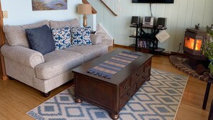 A living room with a sofa, coffee table, TV, speakers, and a wood-burning stove. - Hood Canal "Seaside Chalet". Beautifully updated and decorated.  Lovely setting! (Belfair)