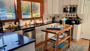 A modern kitchen with a wooden island, stainless steel appliances, and a view through large windows. - Hood Canal "Seaside Chalet". Beautifully updated and decorated.  Lovely setting! (Belfair)