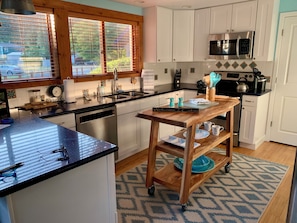 A modern kitchen with a wooden island, stainless steel appliances, and a view through large windows.
