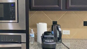 Eine Küche mit dunklen Schränken, Edelstahlgeräten, einer Kaffeemaschine und einer Wasserflasche auf der Arbeitsfläche.