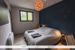 Une chambre moderne avec un grand lit, une fenêtre, un luminaire original et un radiateur.