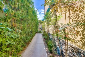 Un étroit sentier bordé d’une végétation luxuriante et un bâtiment doté d’un mur en pierre.