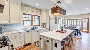 A spacious kitchen with white cabinetry, a large island with bar stools, and a hanging light fixture.
