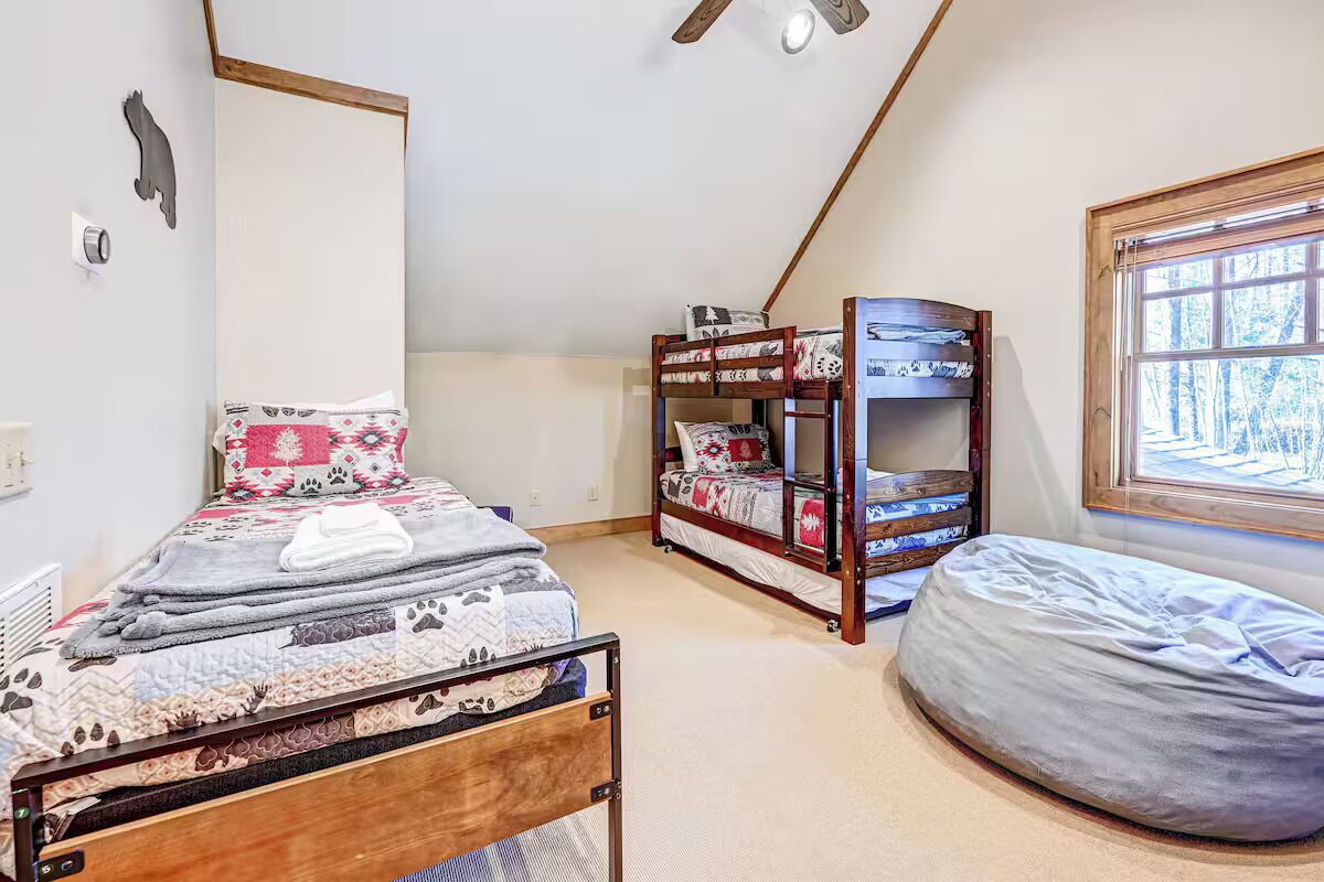 A cozy bedroom with a bunk bed, a bean bag, and a window with a view of trees.