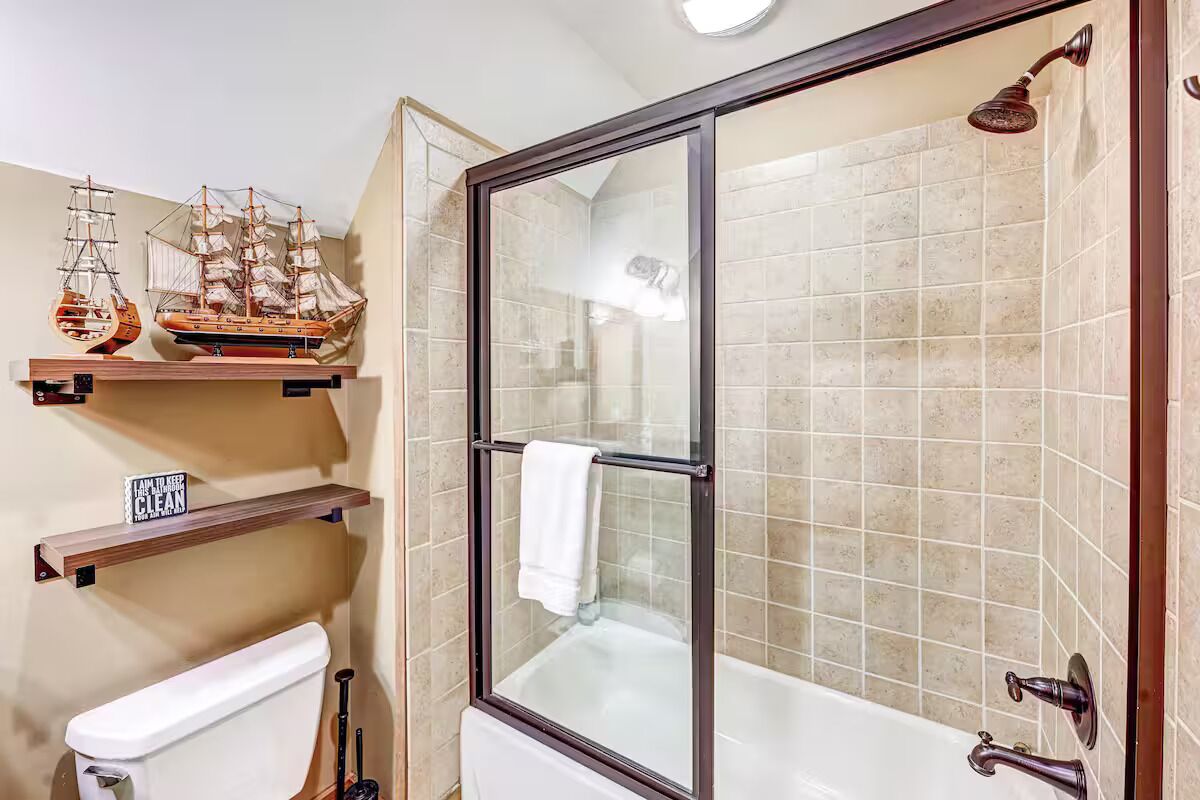 Casa de banho com chuveiro envidraçado, banheira e prateleiras de madeira com objetos decorativos.