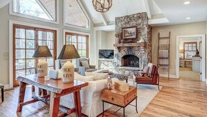 A spacious living room with a stone fireplace, large windows, and a wooden dining table.