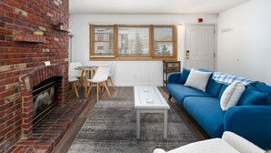 En stue med en murstenspejs, en blå sofa, et hvidt sofabord og et spiseområde med et bord og stole.