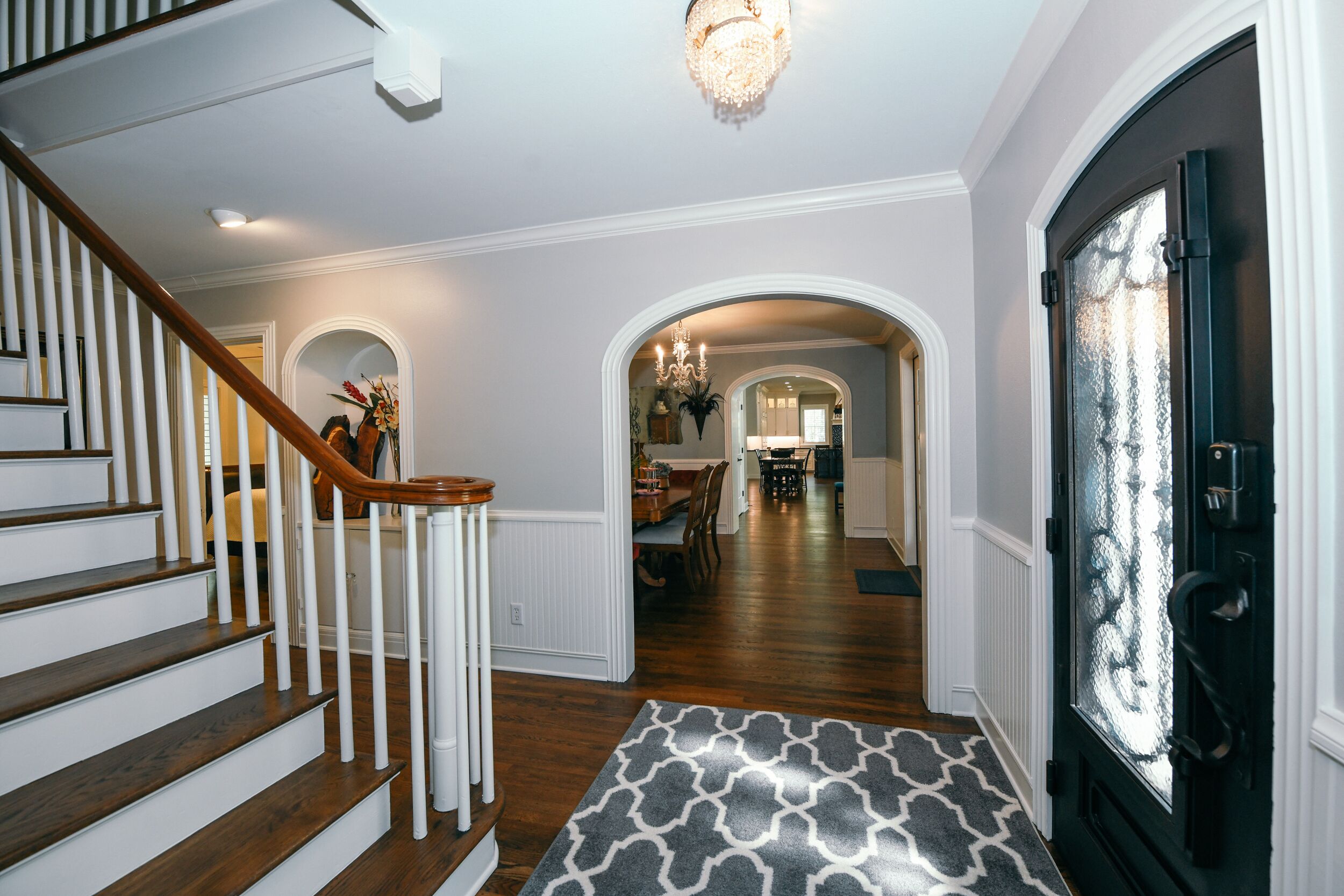 A staircase leading to a dining area with a chandelier, wooden railing, and a patterned rug.