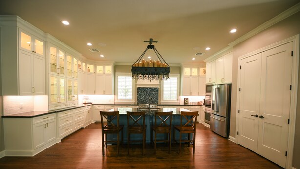 A spacious kitchen with white cabinetry, a central island with chairs, a chandelier, and a refrigerator. - Remodeled Aggieland Historic Home/Gameday Retreat (College Station)