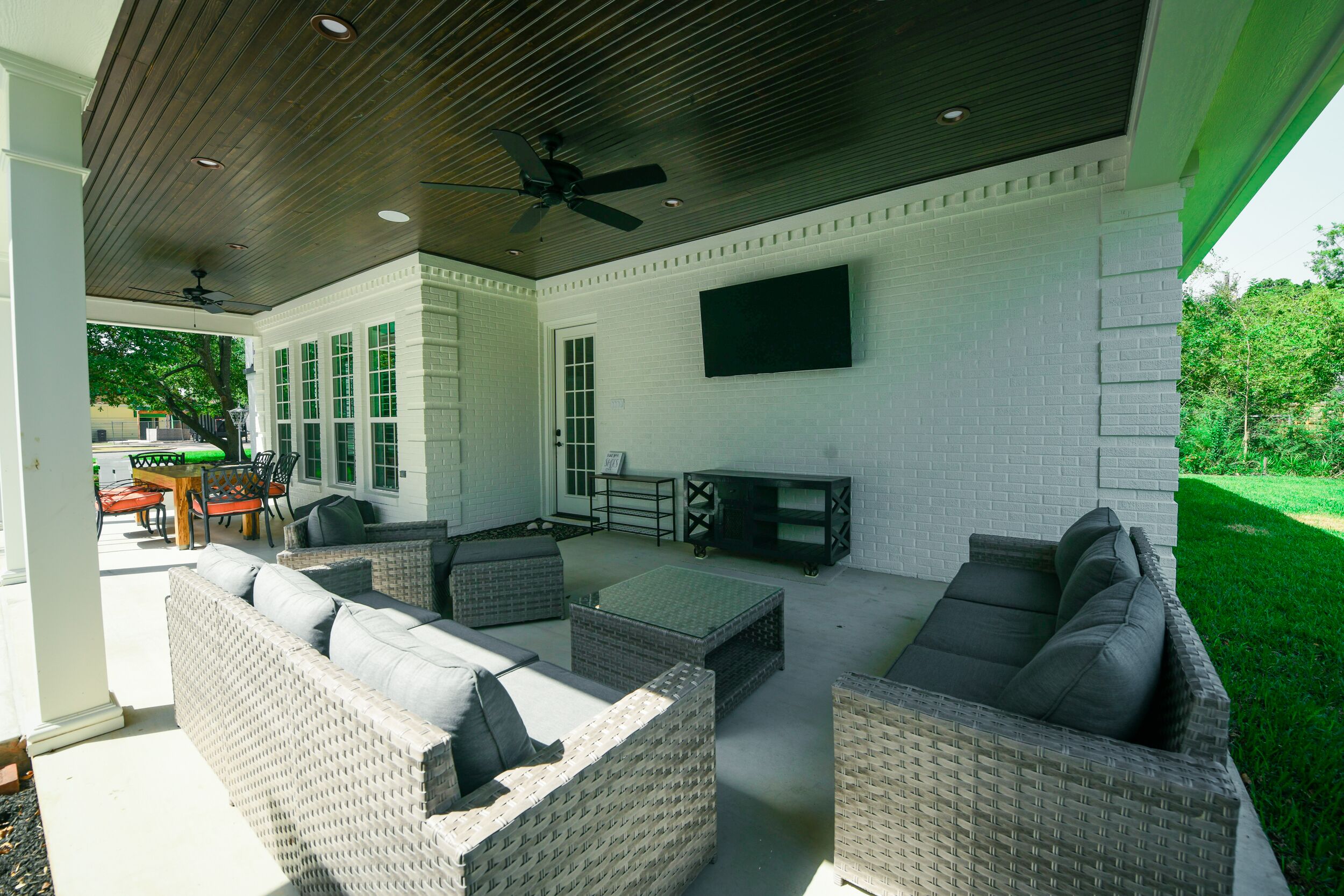 An outdoor patio with wicker furniture, a ceiling fan, and a flat-screen TV mounted on the wall.