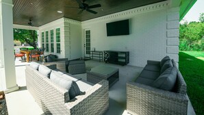An outdoor patio with wicker furniture, a ceiling fan, and a flat-screen TV mounted on the wall. - Remodeled Aggieland Historic Home/Gameday Retreat (College Station)