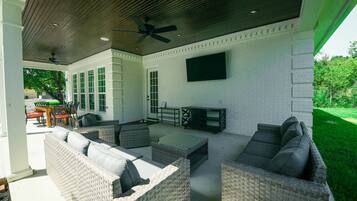 An outdoor patio with wicker furniture, a ceiling fan, and a flat-screen TV mounted on the wall.