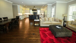 A spacious living room with a dining area, a kitchen in the background, and a red rug. - Remodeled Aggieland Historic Home/Gameday Retreat (College Station)