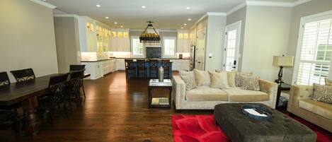 A spacious living room with a dining area, a kitchen in the background, and a red rug.