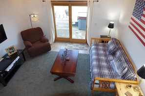 A living room with a brown armchair, a plaid sofa, a wooden coffee table, and a television on a stand. - Whispering Pines Lakehouse - private dock and free zipline and railroad passes (Bryson City)