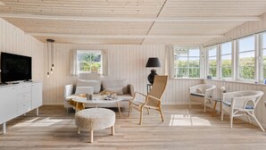 A modern living room with a wooden ceiling, white furniture, and large windows offering a view of greenery. - Lovely home in Bjert with kitchen (Bjert)