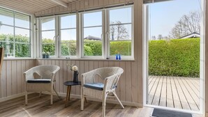 A room with two wicker chairs, a small table, and large windows offering a view of a wooden deck and greenery outside. - Lovely home in Bjert with kitchen (Bjert)