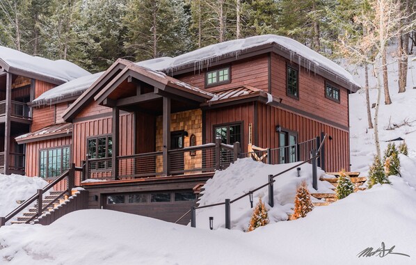 Une cabane en bois à plusieurs étages, dotée d’un porche couvert et d’un escalier menant à l’entrée.