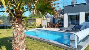 A modern outdoor pool area with a palm tree, lounge chairs, and a table. - 4 * vacation home between La Torche and Pors Carn with swimming pool. (Penmarch)