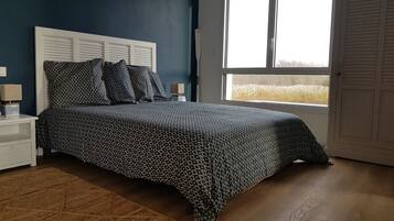 A bedroom with a patterned bedspread, a white headboard, a nightstand with a lamp, and a window with a view of a field.