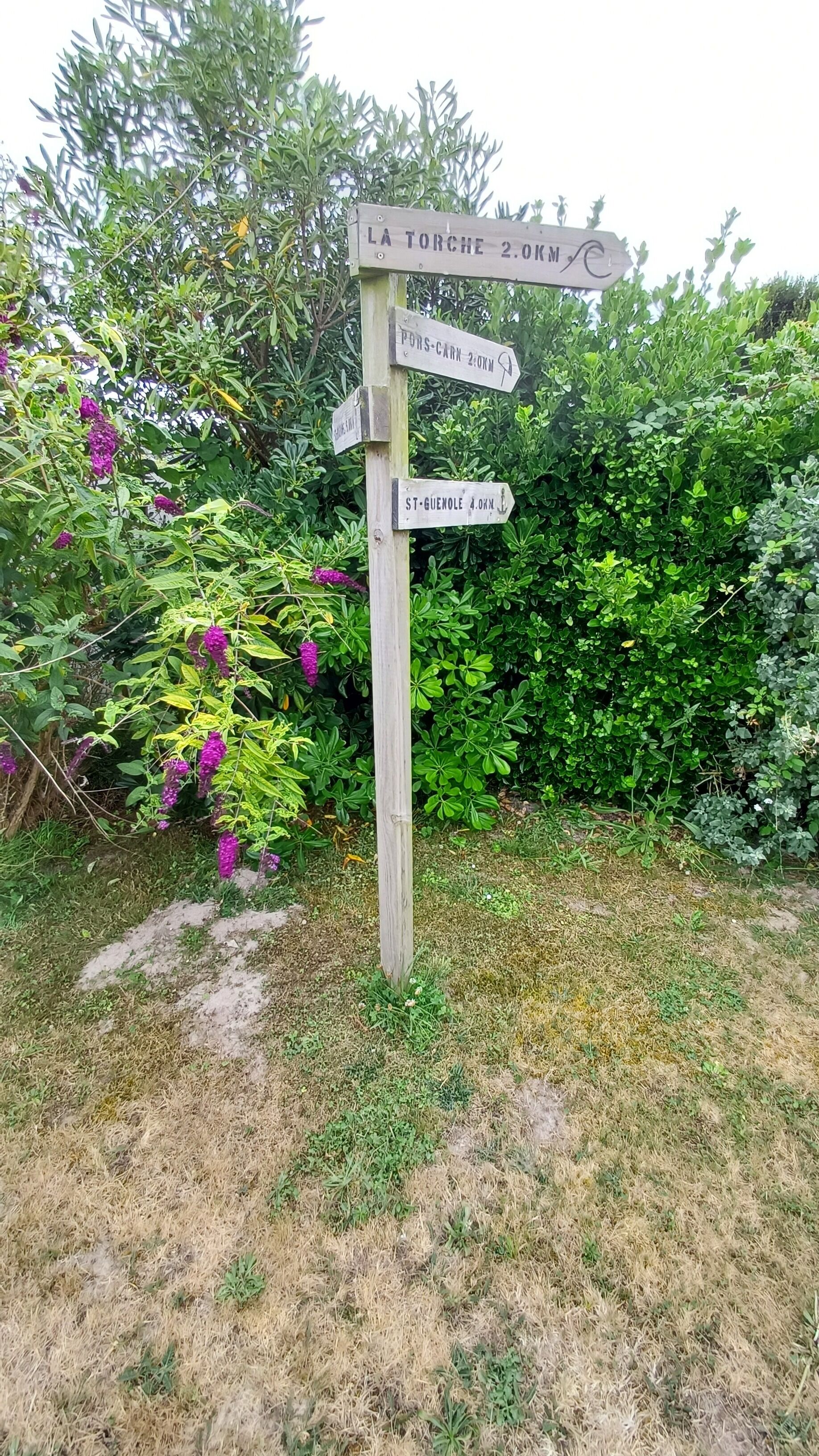 A wooden signpost with directional arrows pointing to La Torche, Pors-Carn, and St. Guenole, indicating distances of 2.0km and 4.0km respectively.