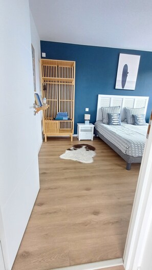 A bedroom with a bed, a nightstand, a wooden wardrobe, a white rug, and a blue wall. - 4 * vacation home between La Torche and Pors Carn with swimming pool. (Penmarch)