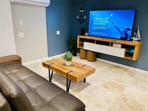 Un salon moderne avec un canapé en cuir, une table basse en bois agrémentée d’une plante, un téléviseur fixé sur un mur bleu et un meuble de rangement en bois.