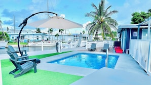 Uma área de piscina com espreguiçadeira, piscina pequena e um cais para barcos.