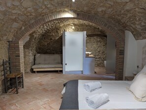Une chambre avec des murs en pierre, un lit avec deux serviettes enroulées, un canapé et une petite table sur laquelle se trouve un bol.