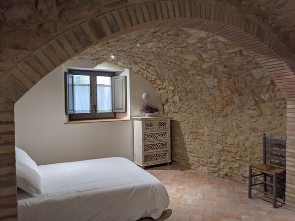 Une chambre avec un plafond voûté en pierre, un lit, une commode et une chaise.