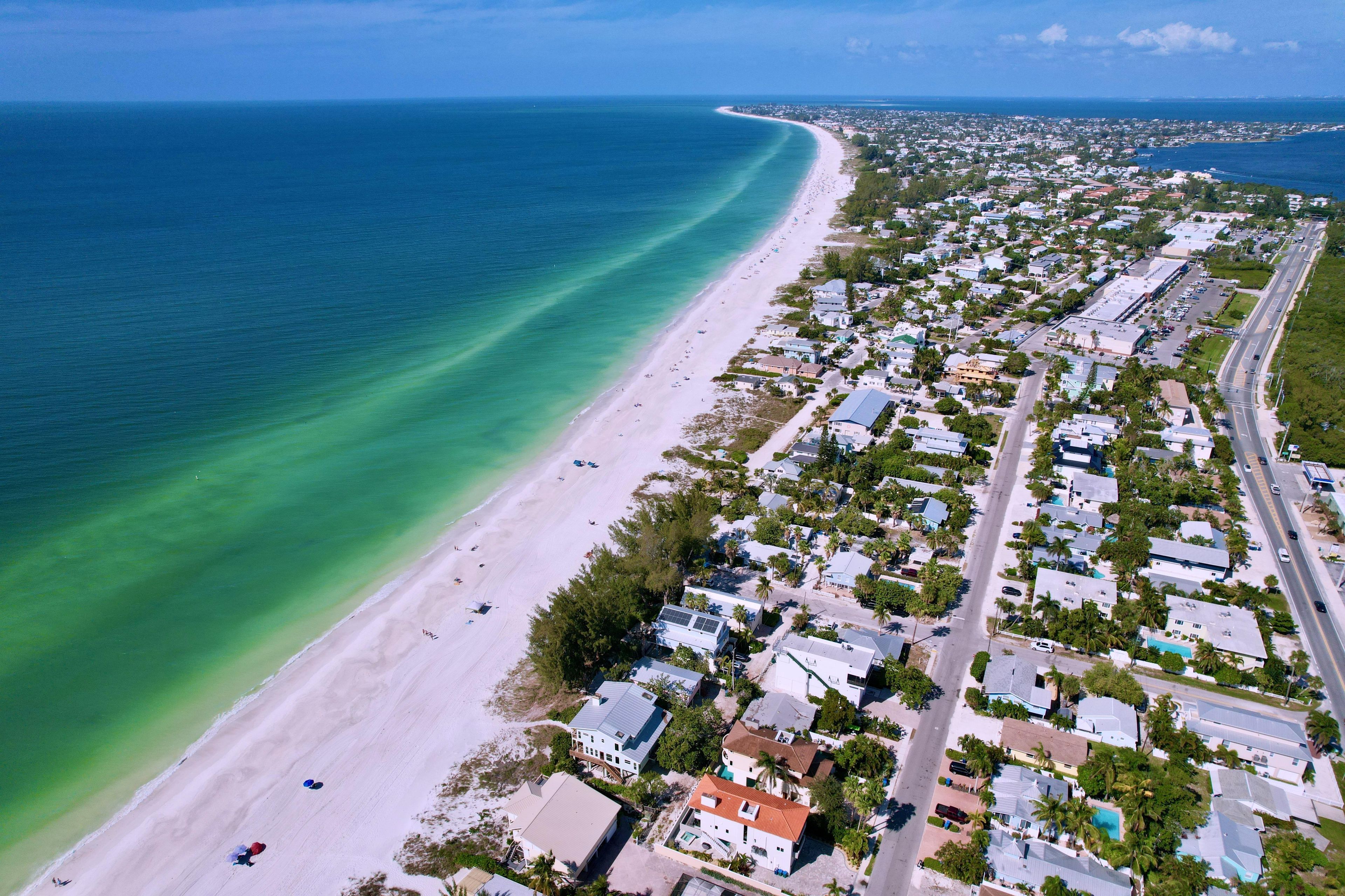 An aerial view of a coastal residential area with a beach, houses, and a road.