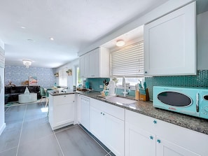 A modern kitchen with white cabinets, a teal backsplash, and a retro-style microwave.