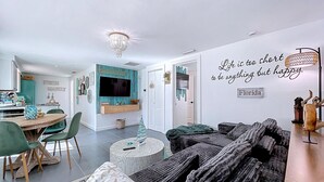 Ett modernt vardagsrum med en stor soffa, en matplats med ett träbord och stolar, en tv som är monterad på en turkosfärgad vägg och ett inspirerande citat på väggen.