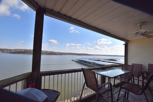 Une terrasse couverte avec vue sur un lac et un quai, comprenant une table et des chaises.
