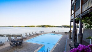 A swimming pool with lounge chairs and tables, surrounded by a white fence, overlooking a body of water. - Large, Beautifully Furnished -Sleeps 12,  6 beds -2 kings & 4 queens -BLDG 10 (Osage Beach)